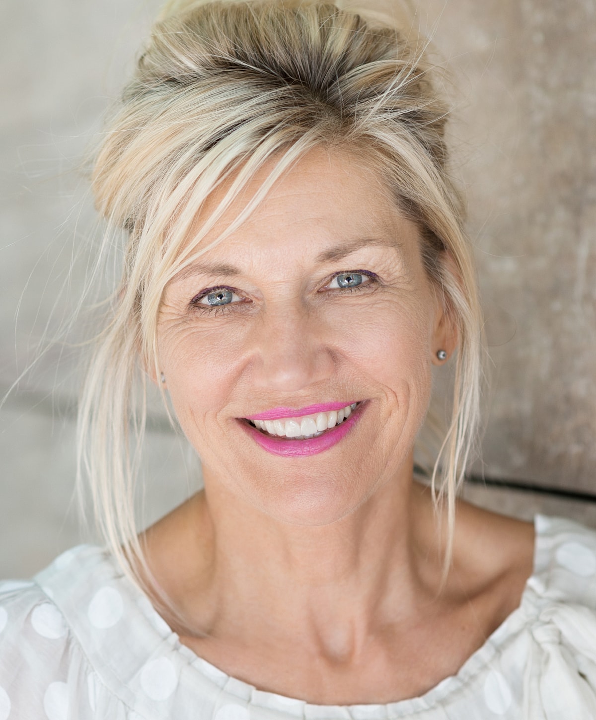 Smiling woman with blonde hair and pink lipstick.
