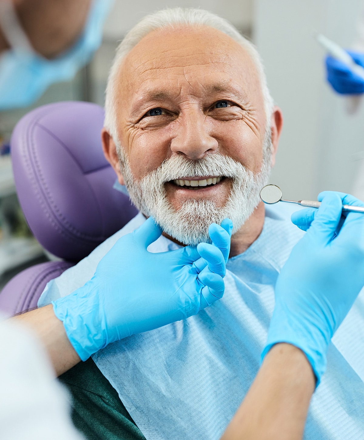 Elderly man smiling in dental check-up chair.